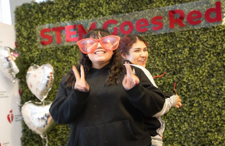 Two girls making peace signs in front of STEM goes red sign