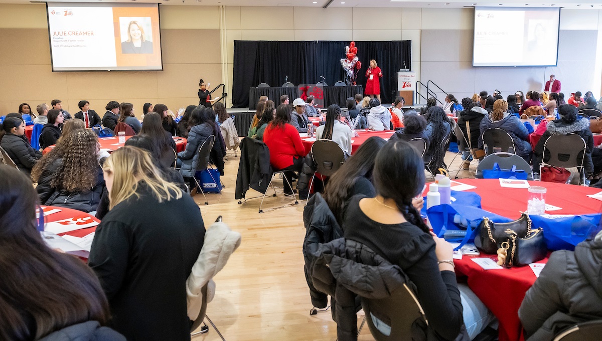 Room full of round tables filled with teenagers listening to speaker Julie Creamer on stage. Room full of round tables filled with teenagers listening to speaker Julie Creamer on stage.